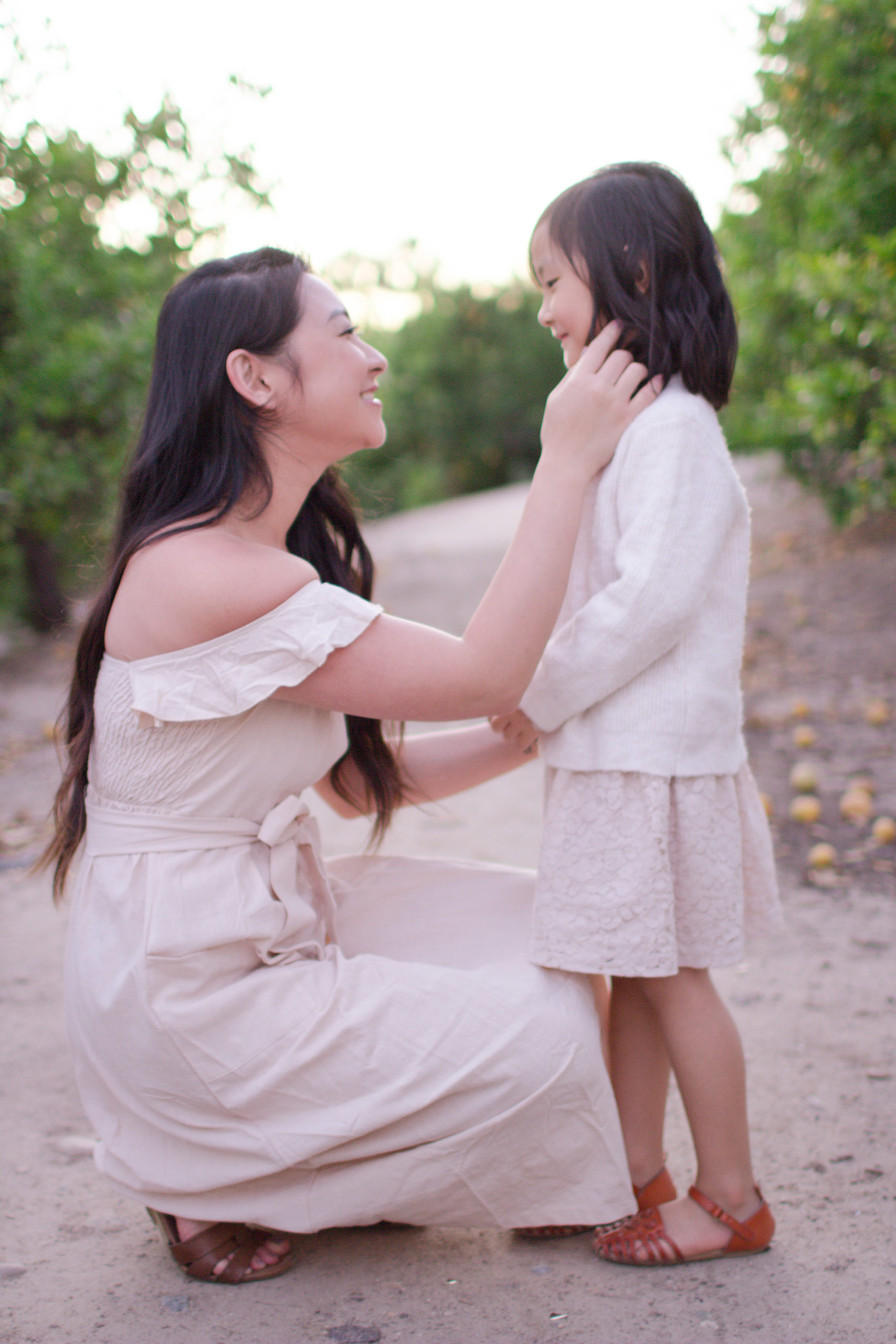 Mother kneels and touches daughter's face. Tiffany Chi Photography